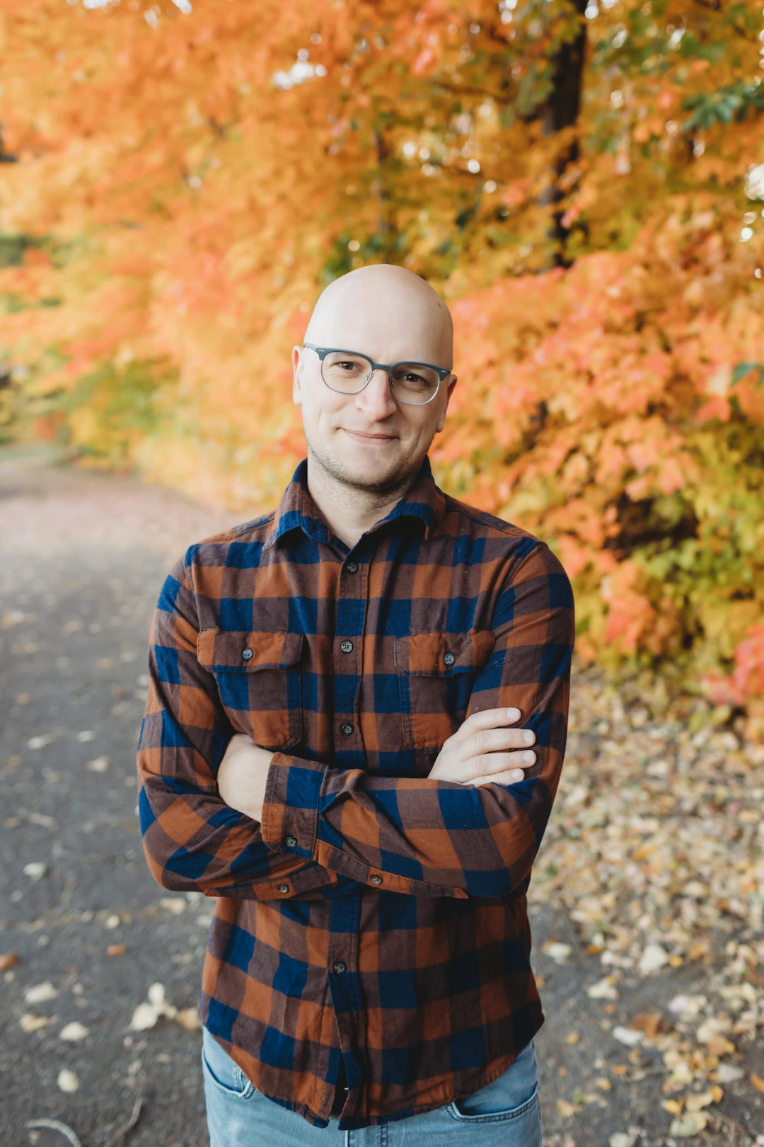 Target Principal Engineer Brian Muenzenmeyer, a man with light skin, wearing glasses and a button down flannel shirt and smiling with his arms crossed against a background of colorful fall leaves