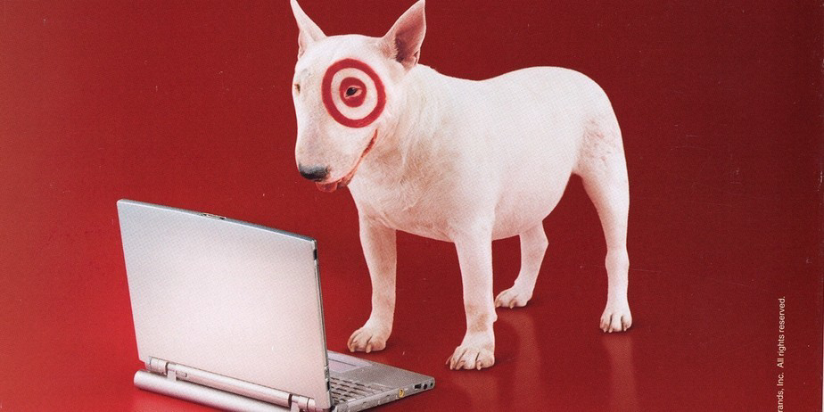 image of Target mascot Bullseye, a white bull terrier with a red target around his eye, looking at an open laptop against a red background