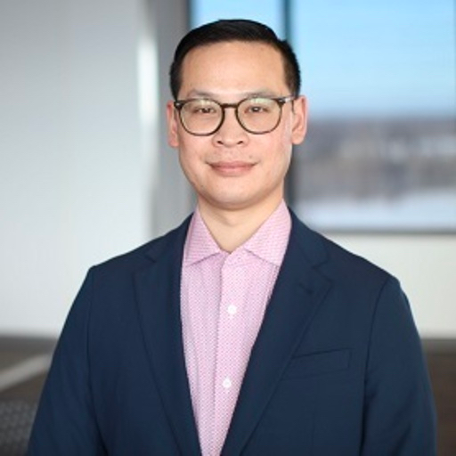 Target Cybersecurity Analyst Dat Dang, pictured smiling against a corporate conference room background, wearing eyeglasses, a button-down shirt, and navy blue blazer